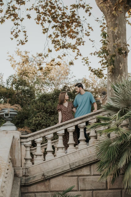 Together on the stone staircase | Barcelona couple photoshoot The couple standing close together on a stone staircase beneath leafy trees during their couple photoshoot in Barcelona.