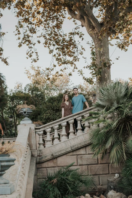 Together on the stone staircase | Barcelona couple photoshoot The couple standing close together on a stone staircase beneath leafy trees during their couple photoshoot in Barcelona.