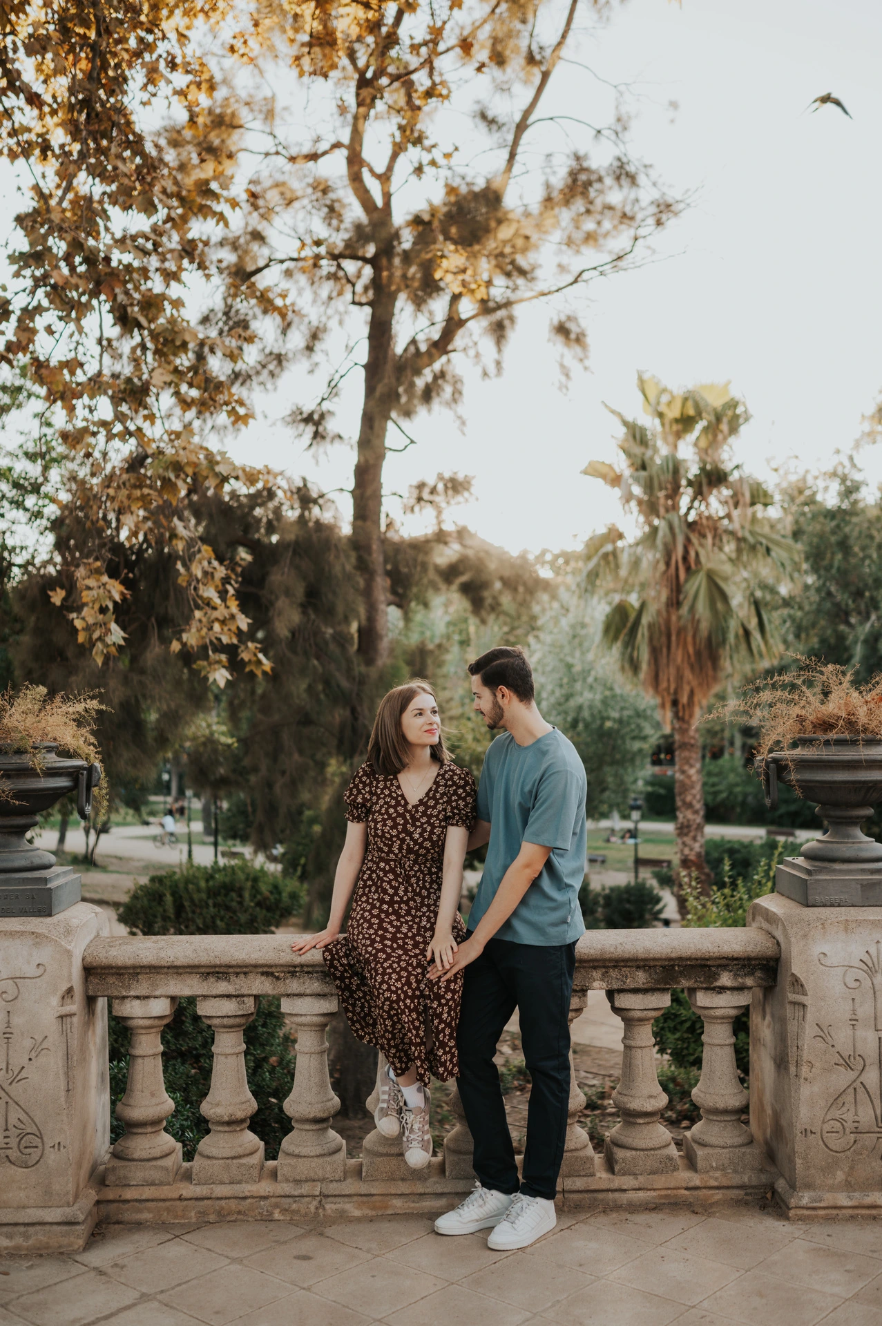 The couple facing each other beside the park balustrade and carved stone urns during their couple photoshoot in Barcelona.
