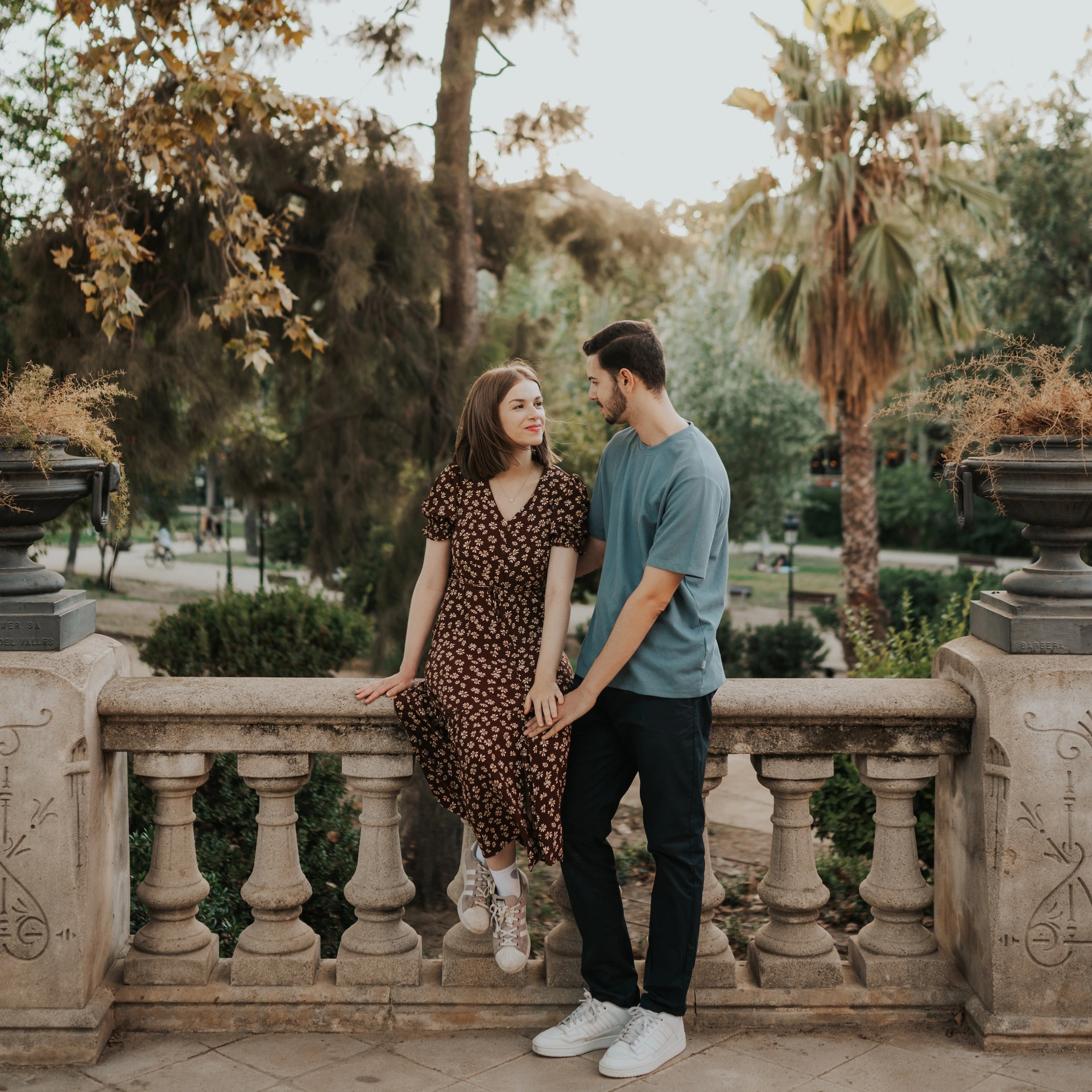 The couple facing each other beside the park balustrade and carved stone urns during their couple photoshoot in Barcelona.