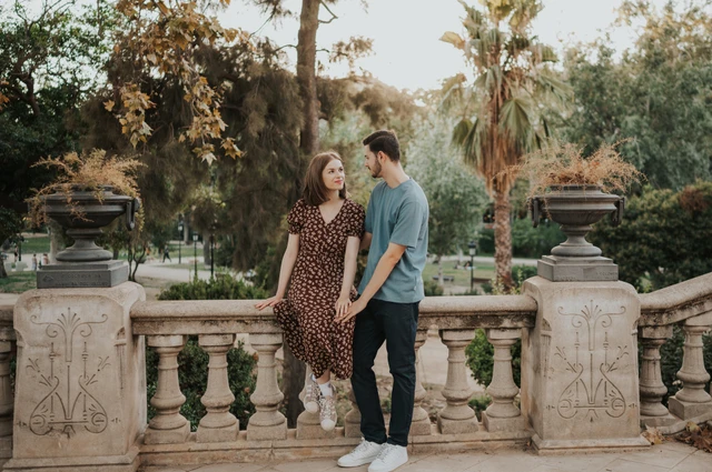 The couple facing each other beside the park balustrade and carved stone urns during their couple photoshoot in Barcelona.