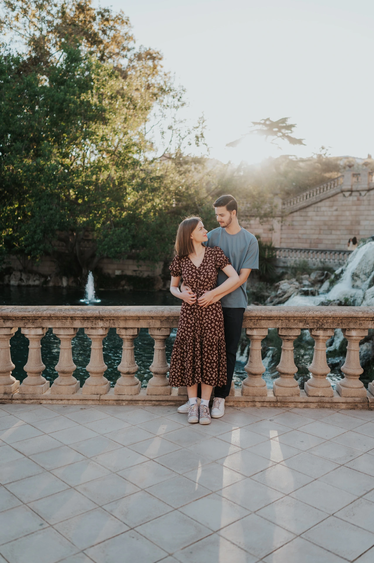The couple holding each other beside the stone balustrade, with the waterfall behind them during their couple photoshoot in Barcelona.