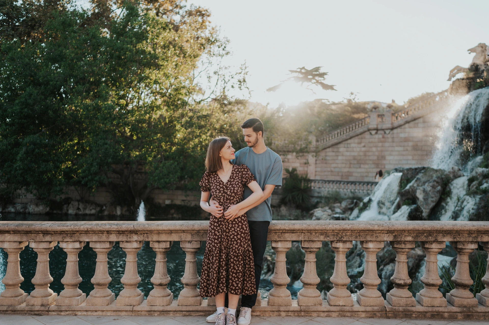 The couple holding each other beside the stone balustrade, with the waterfall behind them during their couple photoshoot in Barcelona.