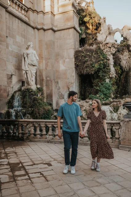 A walk past the waterfall | Barcelona couple photoshoot The couple walking together on the stone paving beside the fountain and waterfall during their couple photoshoot in Barcelona.