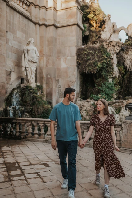 A walk past the waterfall | Barcelona couple photoshoot The couple walking together on the stone paving beside the fountain and waterfall during their couple photoshoot in Barcelona.