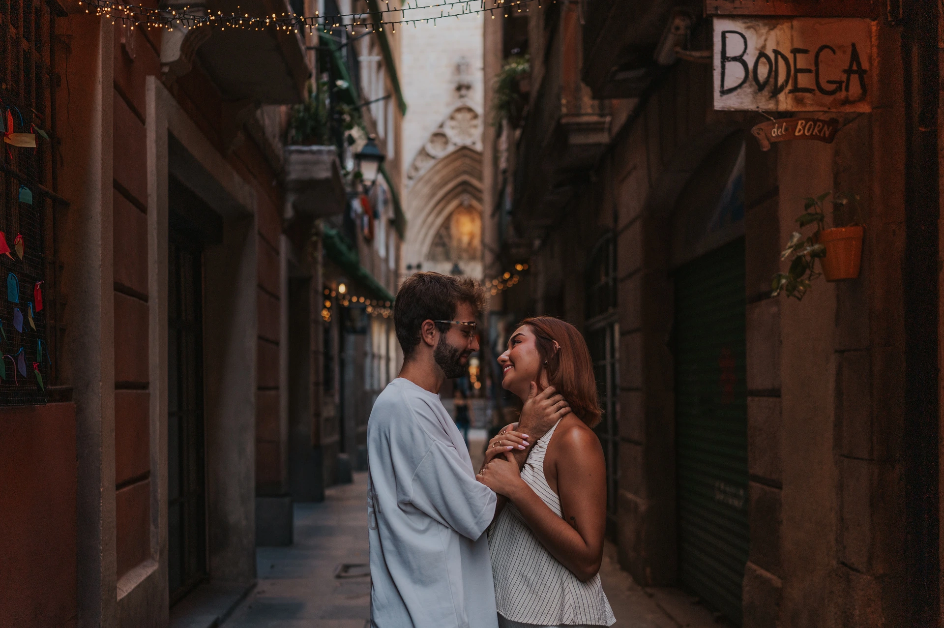 The couple standing close together in a narrow lane, with the Bodega del Born sign above them during their couple photoshoot in Barcelona.