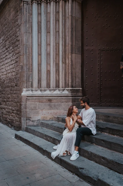 Together on the old church steps | Barcelona couple photoshoot The couple sitting together on stone church steps beside a tall carved column and a wooden door during their couple photoshoot in Barcelona.