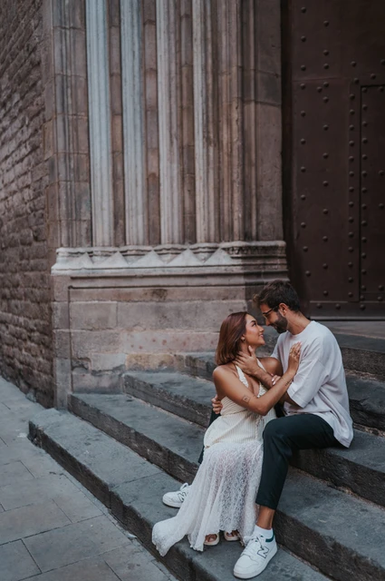 A close portrait beside the church doorway | Barcelona couple photoshoot The couple sitting face to face on stone church steps, with carved stonework behind them during their couple photoshoot in Barcelona.