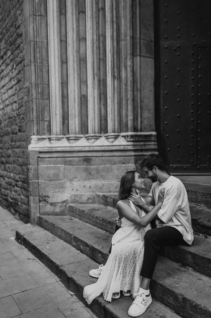 Close together on the stone steps in black and white | Barcelona couple photoshoot Black-and-white photograph of a close view of the couple sitting together on stone church steps beside a carved column during their couple photoshoot in Barcelona.