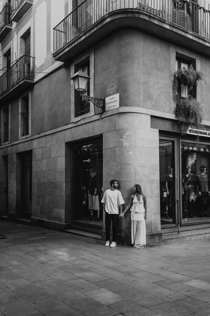 Together at an old town street corner in black and white | Barcelona couple photoshoot Black-and-white photograph of the couple standing hand in hand beneath a street lamp on the corner of a historic building during their couple photoshoot in Barcelona.