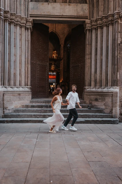 Hand in hand by the Gothic entrance | Barcelona couple photoshoot The couple moving hand in hand across a Gothic church entrance with its tall doors open behind them during their couple photoshoot in Barcelona.