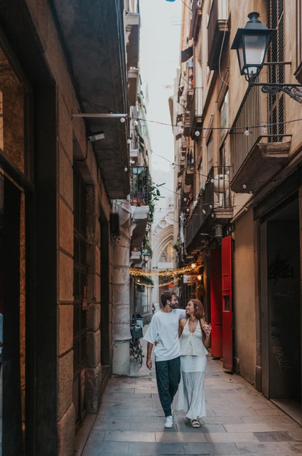 A walk beneath the old street lamps | Barcelona couple photoshoot The couple walking side by side through a narrow lane beneath old lamps and small balconies during their couple photoshoot in Barcelona.
