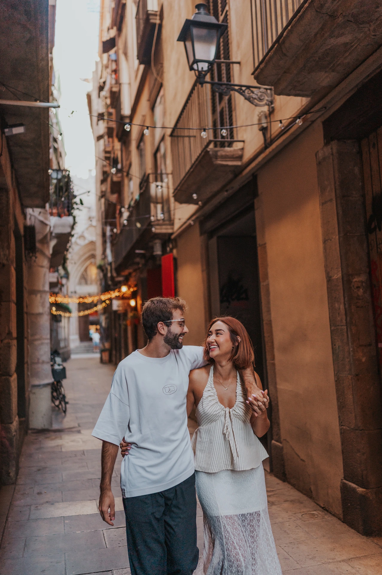 The couple walking close together along a narrow lane with balconies and an old street lamp during their couple photoshoot in Barcelona.