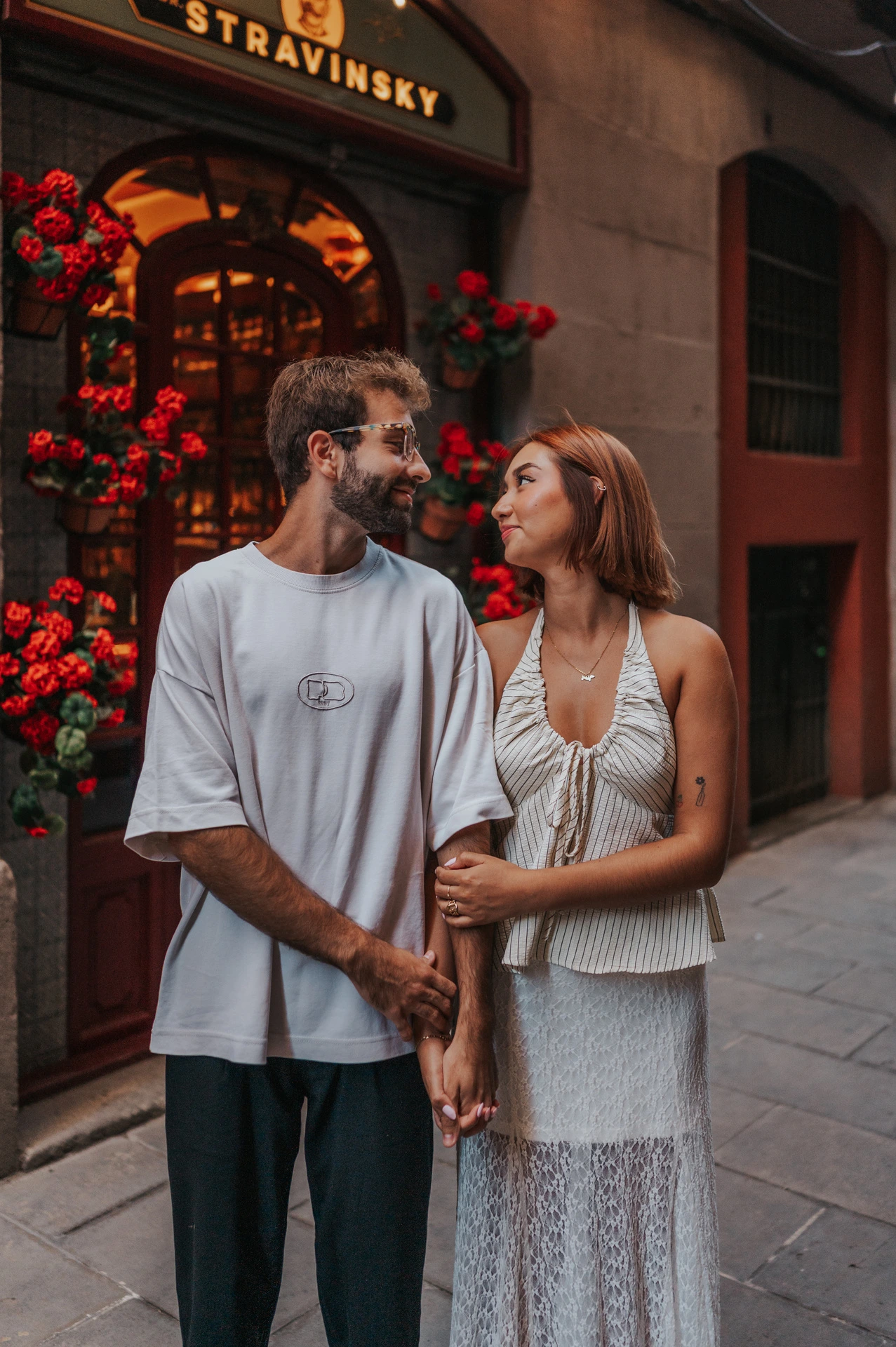 The couple standing close together beside a doorway decorated with red flowers during their couple photoshoot in Barcelona.