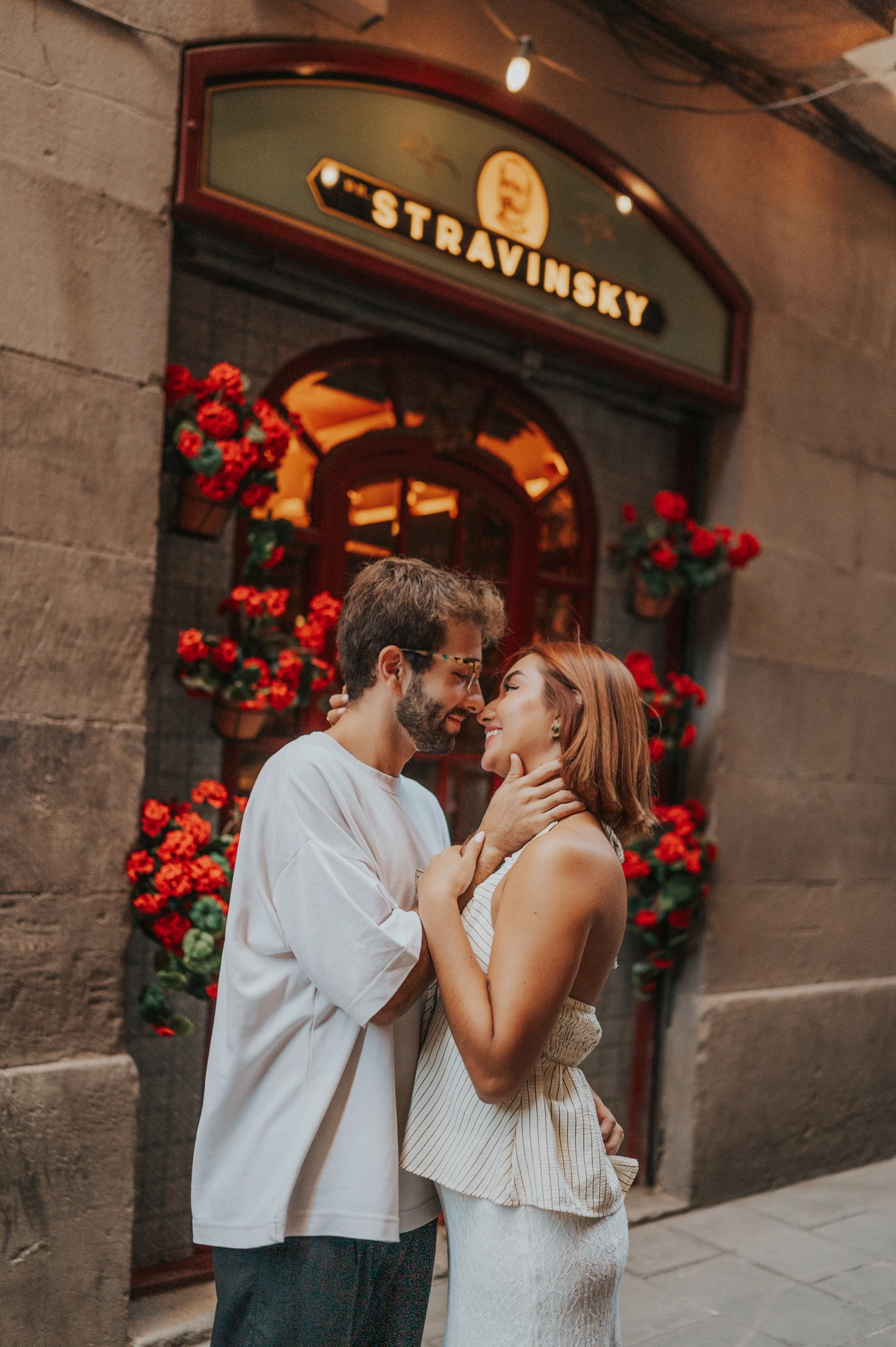 A close view of the couple leaning together beside a doorway decorated with red flowers during their couple photoshoot in Barcelona.