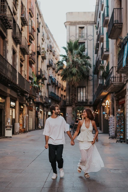 Hand in hand among the shopfronts | Barcelona couple photoshoot The couple walking hand in hand along a paved street lined with shops and historic façades during their couple photoshoot in Barcelona.