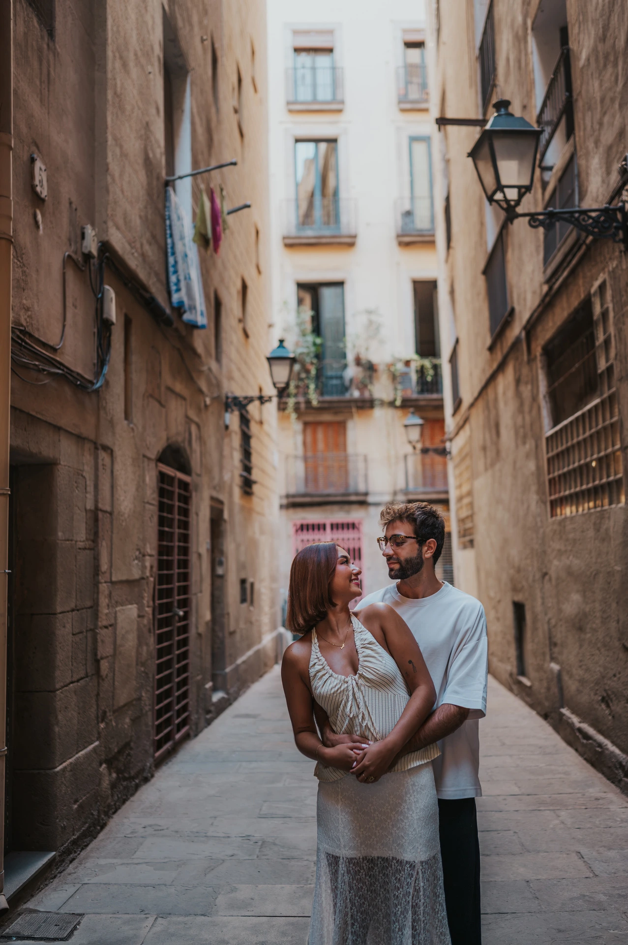 The man embracing his partner from behind in a narrow stone lane during their couple photoshoot in Barcelona.