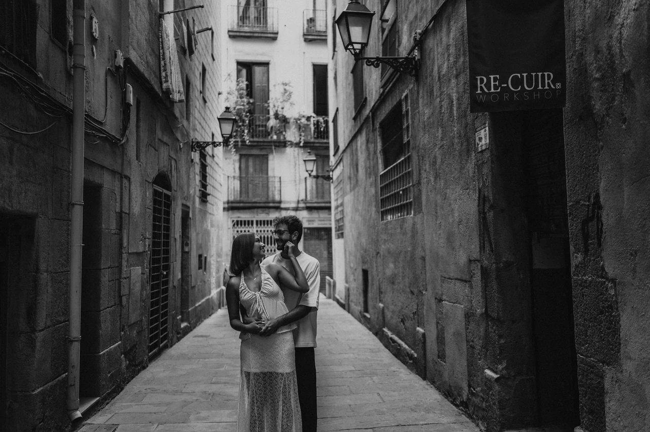 Together between the old stone walls in black and white | Barcelona couple photoshoot Black-and-white photograph of a wide view of the couple embracing between the tall walls of a narrow stone lane during their couple photoshoot in Barcelona.