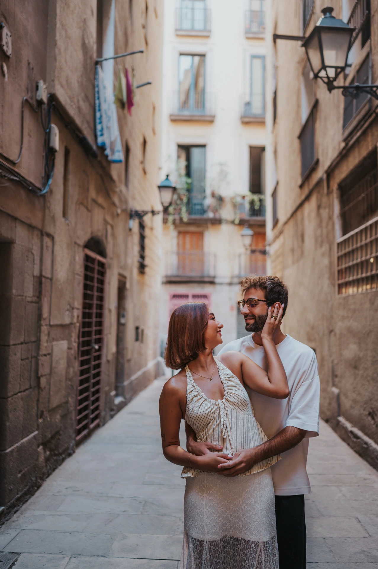 The woman resting her hand on her partner’s cheek as they stand close together in a stone lane during their couple photoshoot in Barcelona.