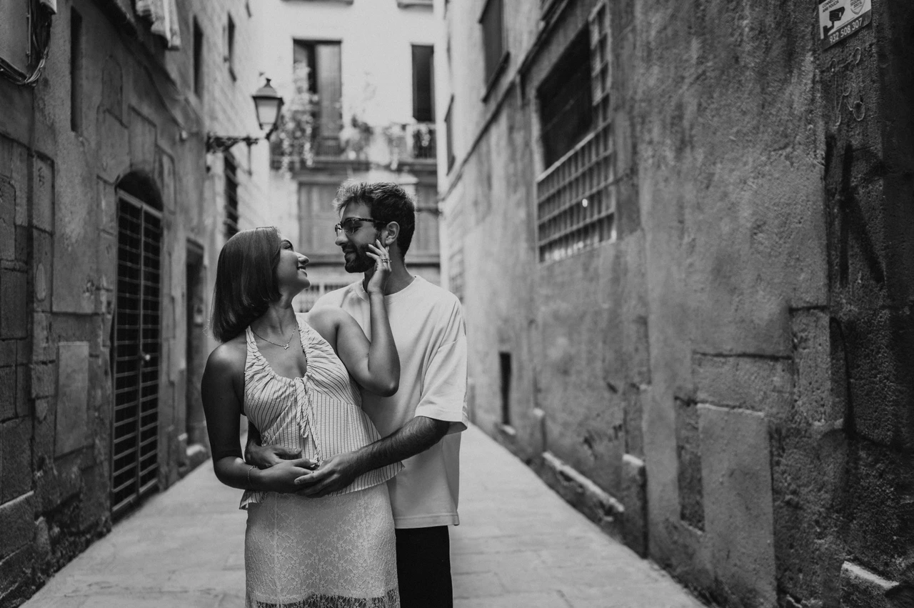 A close embrace in the old town in black and white | Barcelona couple photoshoot Black-and-white photograph of the couple embracing in a stone lane, with the woman’s hand resting on her partner’s cheek during their couple photoshoot in Barcelona.