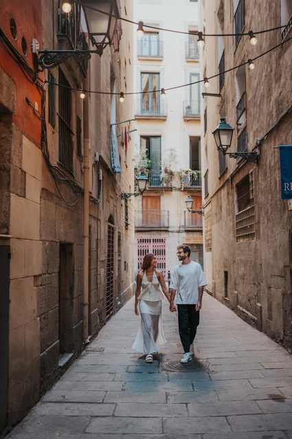 The couple walking hand in hand through a narrow stone lane beneath old street lamps during their couple photoshoot in Barcelona.