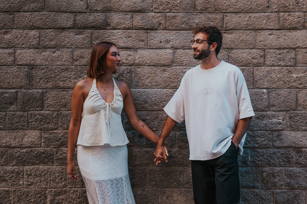 Holding hands beside a stone wall | Barcelona couple photoshoot The couple looking at each other while holding hands against a textured stone wall during their couple photoshoot in Barcelona.