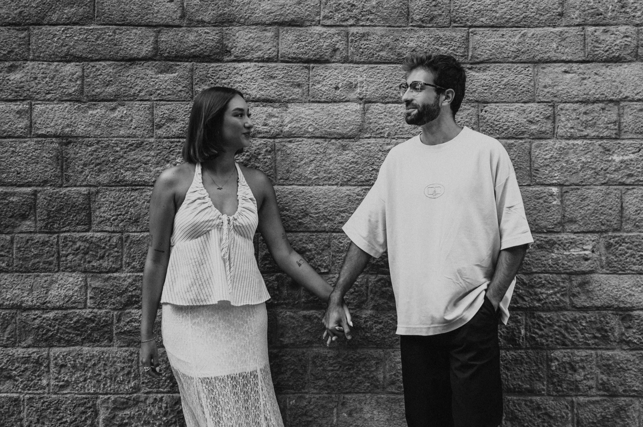 Smiling together against old stone in black and white | Barcelona couple photoshoot Black-and-white photograph of the couple smiling at each other while holding hands beside a textured stone wall during their couple photoshoot in Barcelona.