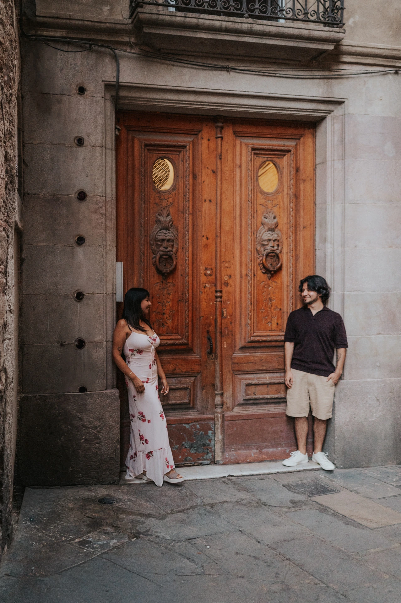 The couple standing on either side of a carved wooden double door in a stone entrance in the Gothic Quarter during their couple photoshoot in Barcelona.