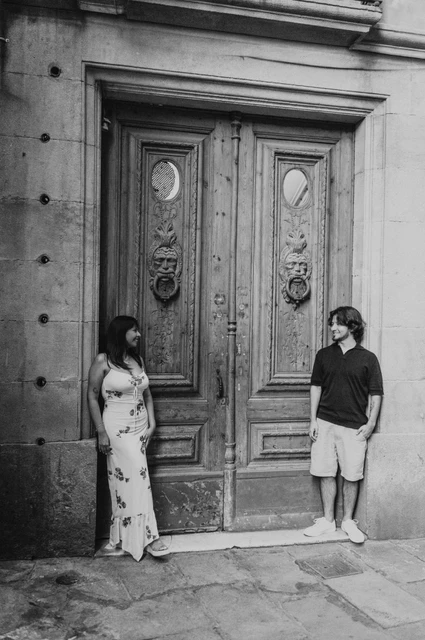 Beside a carved wooden doorway in black and white | Barcelona couple photoshoot Black-and-white photograph: the couple standing on either side of a carved wooden double door in a stone entrance in the Gothic Quarter during their couple photoshoot in Barcelona.