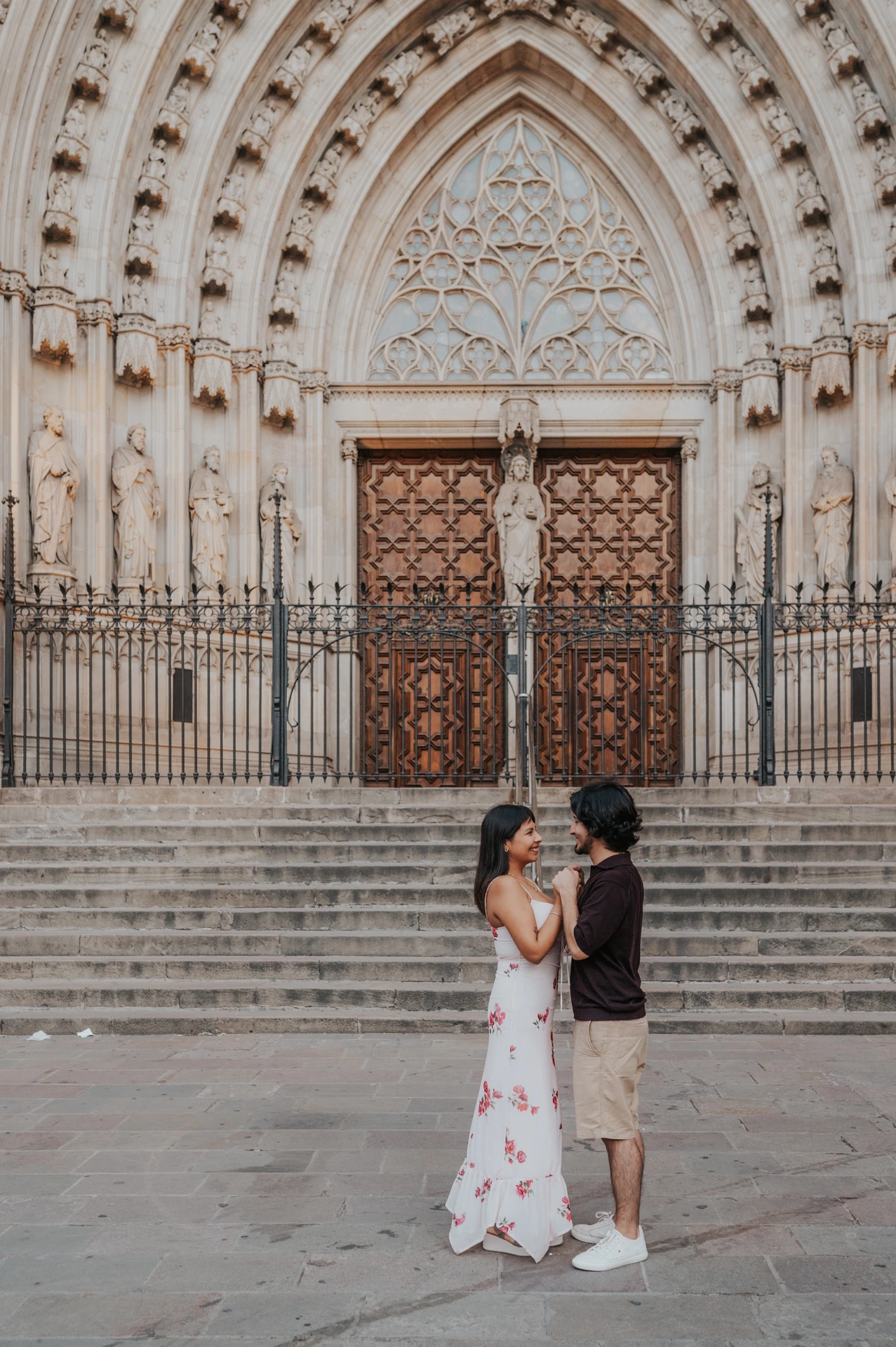 The couple standing face to face and holding hands below the carved doorway of Barcelona Cathedral during their couple photoshoot in Barcelona.