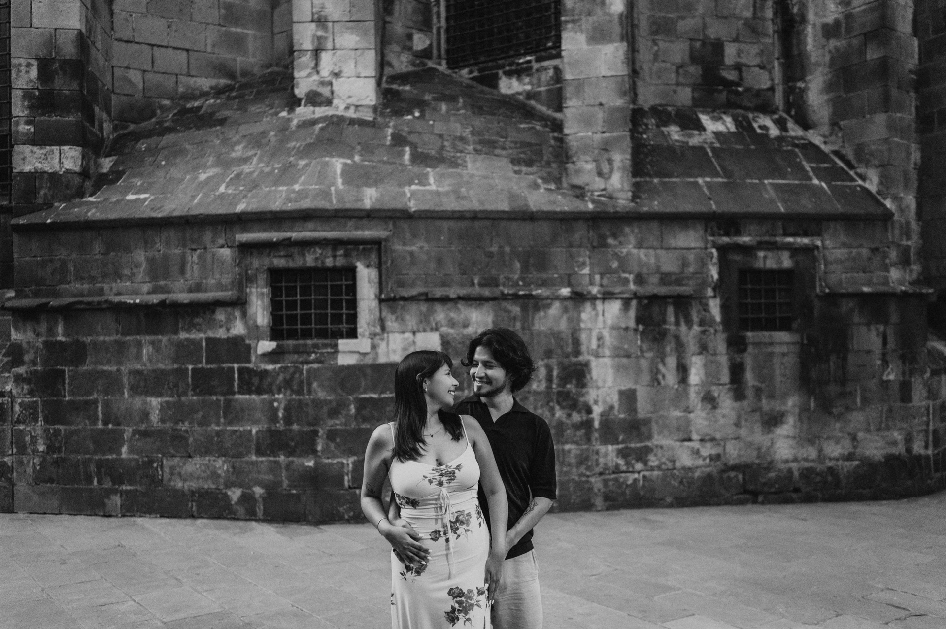 A close portrait against the old stone walls in black and white | Barcelona couple photoshoot Black-and-white photograph: the couple smiling together in front of a textured stone wall in the Gothic Quarter during their couple photoshoot in Barcelona.