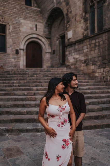 Together below the steps at Plaça del Rei | Barcelona couple photoshoot The couple standing close together and looking to one side, with the broad stone steps at Plaça del Rei behind them during their couple photoshoot in Barcelona.
