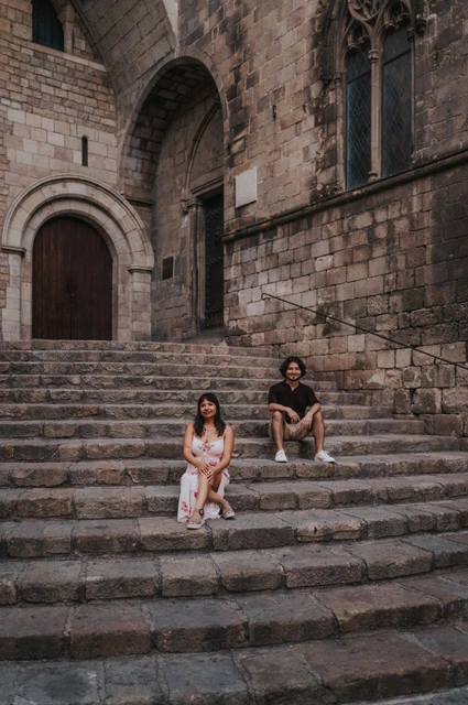 Seated together on the old stone steps | Barcelona couple photoshoot The couple sitting on different levels of the broad stone steps at Plaça del Rei and looking towards the camera during their couple photoshoot in Barcelona.