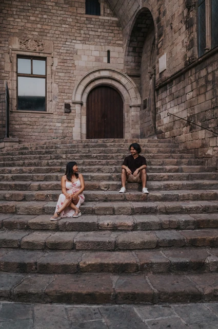 A quiet portrait on the steps of Plaça del Rei | Barcelona couple photoshoot The couple sitting on different levels of the broad stone steps at Plaça del Rei and looking at each other during their couple photoshoot in Barcelona.