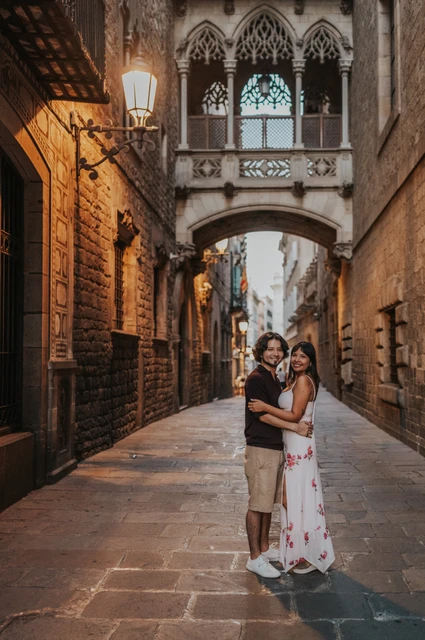 The couple embracing beneath Pont del Bisbe, with glowing lamps along the stone lane during their couple photoshoot in Barcelona.
