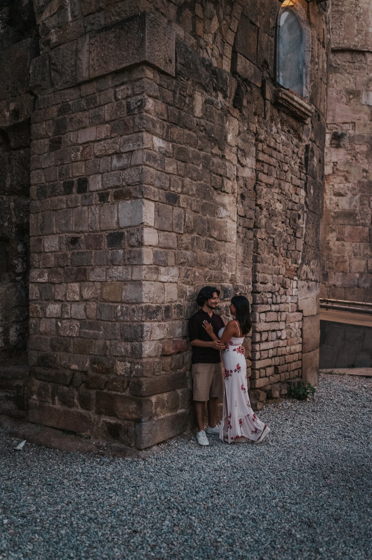 A closer portrait of the couple leaning together at the corner of an old stone building beneath a glowing wall lamp in the Gothic Quarter during their couple photoshoot in Barcelona.