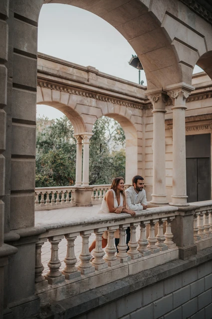 A pause together along the carved railing | Barcelona engagement photoshoot The couple leaning together on the carved stone railing beneath the pavilion arches during their engagement photoshoot in Barcelona.