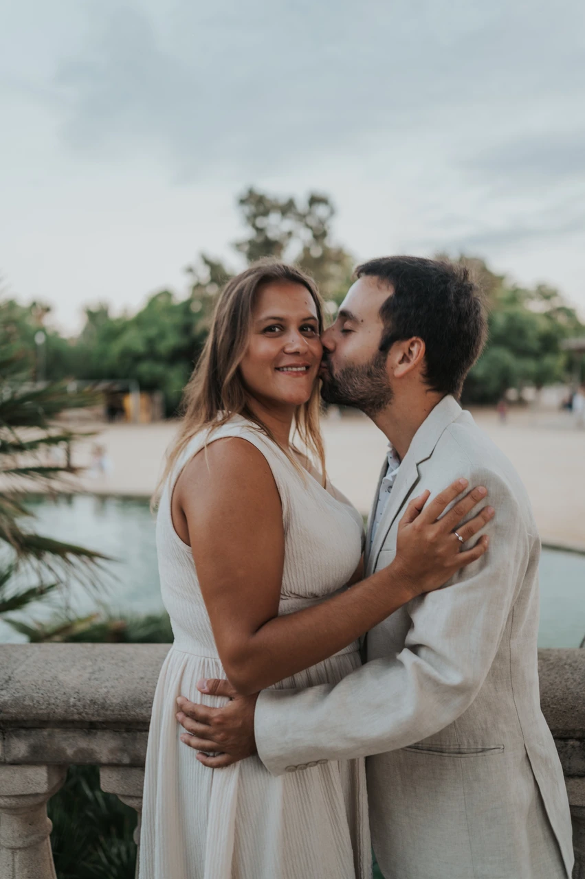 A kiss on the cheek beside the terrace | Barcelona engagement photoshoot The man kissing his partner on the cheek as they embrace beside the stone balustrade during their engagement photoshoot in Barcelona.
