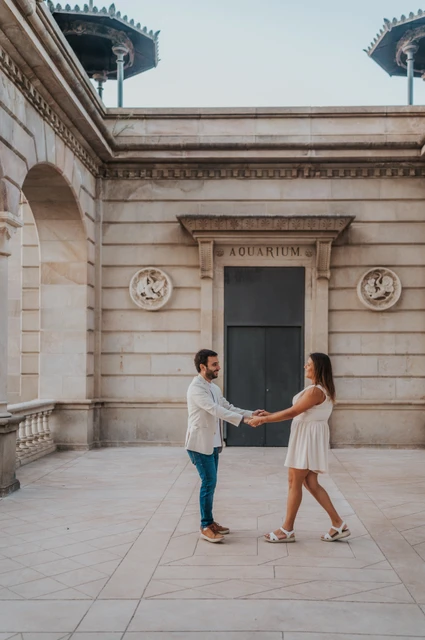 A hand-in-hand turn in the pavilion courtyard | Barcelona engagement photoshoot The couple holding hands as the woman turns towards the man on a paved courtyard beside the pavilion during their engagement photoshoot in Barcelona.