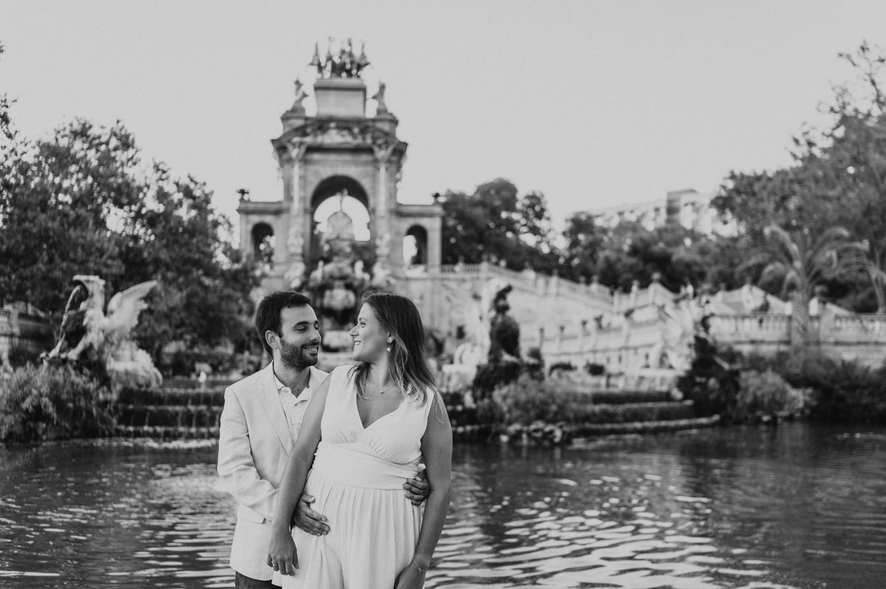 An embrace beside the green fountain pool in black and white | Barcelona engagement photoshoot Black-and-white photograph: the man holding his partner close beside the fountain pool as they look towards each other during their engagement photoshoot in Barcelona.