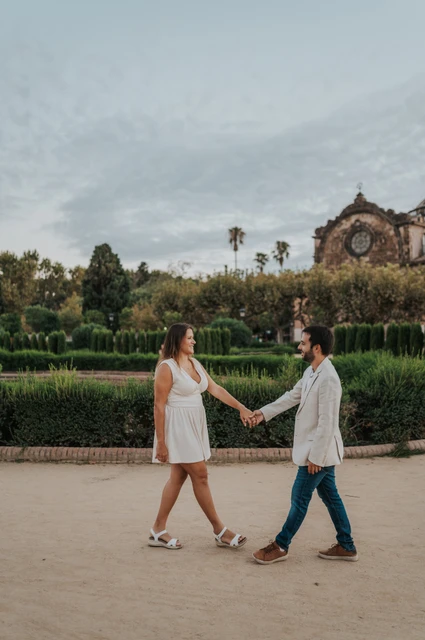 Holding hands across the garden path | Barcelona engagement photoshoot The couple facing each other and holding hands across a broad garden path during their engagement photoshoot in Barcelona.