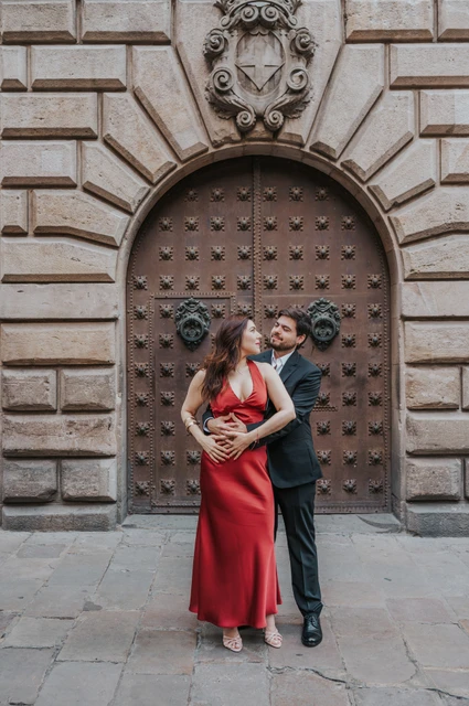 An embrace beside a carved stone doorway | Barcelona engagement photoshoot The man embracing his partner from behind in front of a studded wooden door in the Gothic Quarter during their engagement photoshoot in Barcelona.
