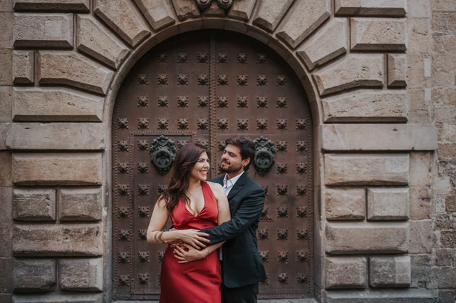 The man embracing his partner from behind in front of a studded wooden door in the Gothic Quarter during their engagement photoshoot in Barcelona.