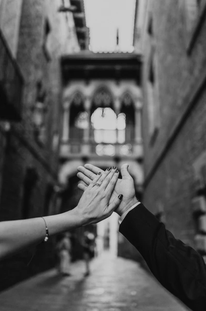 An engagement ring with Pont del Bisbe in the background in black and white | Barcelona engagement photoshoot Black-and-white photograph: a close-up of the couple’s raised hands and engagement ring, with Pont del Bisbe softly blurred behind them during their engagement photoshoot in Barcelona.