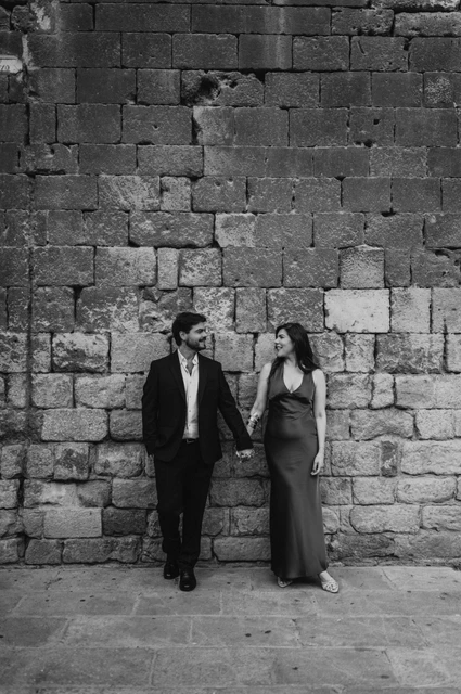 Portraits against the old town’s stone walls in black and white | Barcelona engagement photoshoot Black-and-white photograph: the couple standing together against a textured historic stone wall in the Gothic Quarter during their engagement photoshoot in Barcelona.