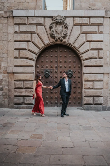 Hand in hand by a Gothic Quarter doorway | Barcelona engagement photoshoot The couple holding hands in front of a large arched wooden door in the Gothic Quarter during their engagement photoshoot in Barcelona.
