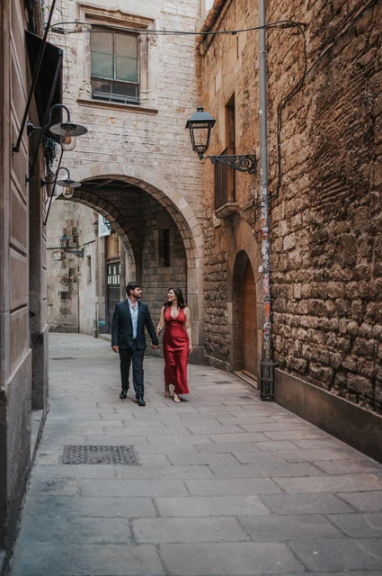 A walk through an arched Gothic Quarter lane | Barcelona engagement photoshoot The couple walking together through a stone lane beneath an arch in the Gothic Quarter during their engagement photoshoot in Barcelona.