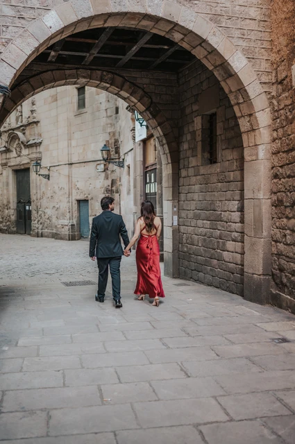 Beneath a broad stone arch in the old town | Barcelona engagement photoshoot The couple walking away hand in hand beneath a broad stone arch in the Gothic Quarter during their engagement photoshoot in Barcelona.
