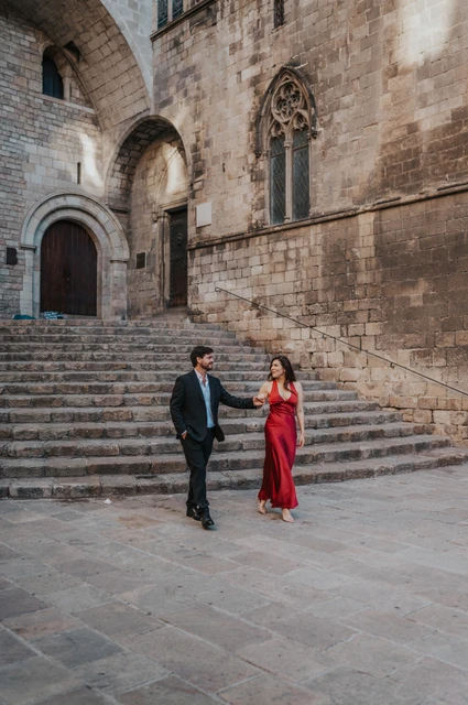 A walk across Plaça del Rei | Barcelona engagement photoshoot The couple walking together across the square below the broad stone steps of Plaça del Rei during their engagement photoshoot in Barcelona.