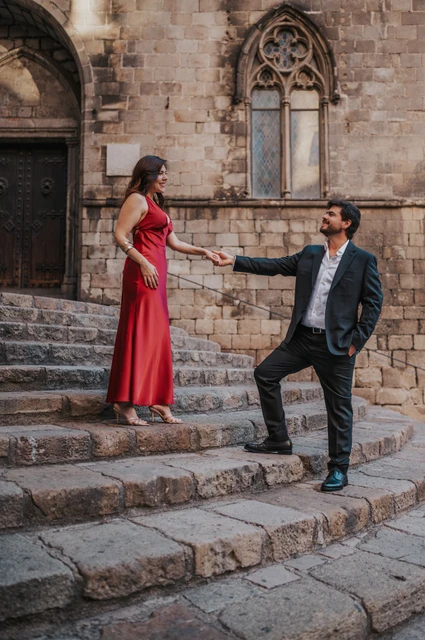 Together on the stone steps of Plaça del Rei | Barcelona engagement photoshoot The couple holding hands on the broad stone steps at Plaça del Rei, with historic doors and pointed windows behind them during their engagement photoshoot in Barcelona.